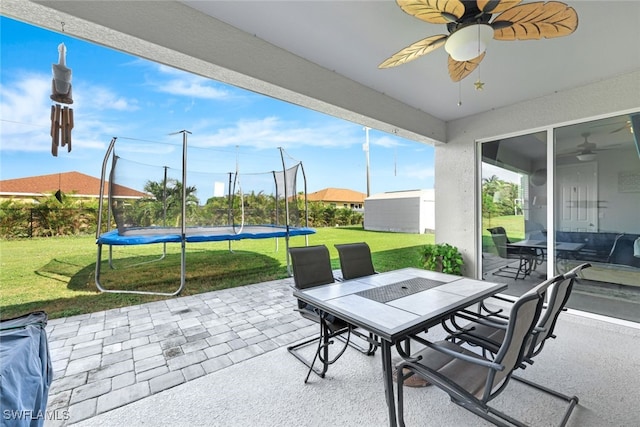 view of patio / terrace with a trampoline, an outbuilding, outdoor dining area, and a ceiling fan