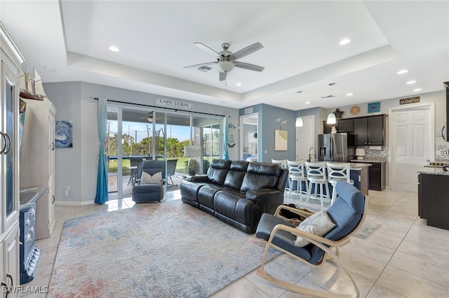 living room featuring light tile patterned floors, ceiling fan, and a tray ceiling