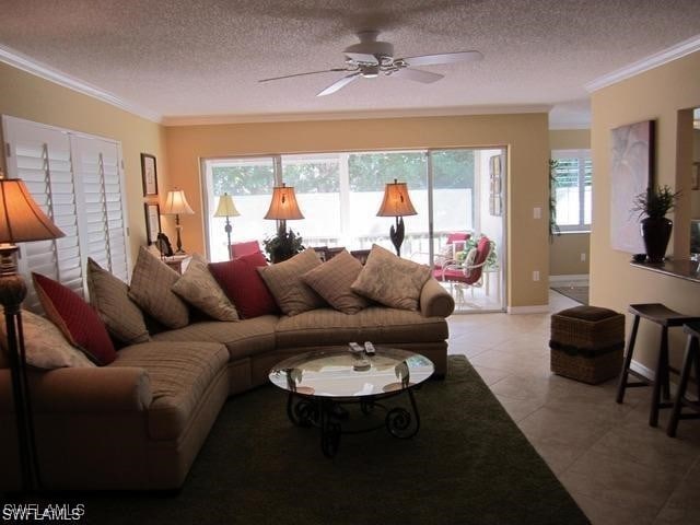 living room with ornamental molding, a ceiling fan, light tile patterned flooring, a textured ceiling, and baseboards