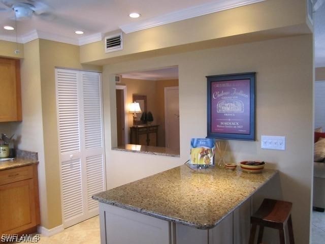 kitchen featuring recessed lighting, a peninsula, visible vents, ornamental molding, and light stone countertops