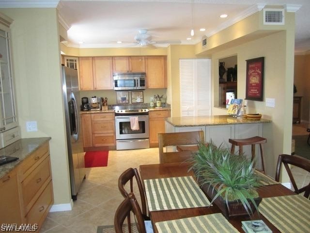 kitchen featuring light stone counters, crown molding, stainless steel appliances, visible vents, and ceiling fan