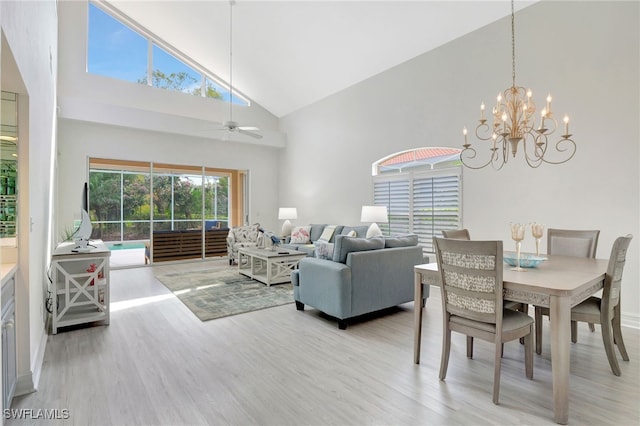 dining room featuring light wood finished floors, ceiling fan with notable chandelier, and high vaulted ceiling