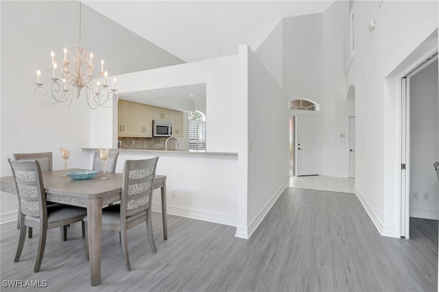 dining space with baseboards, arched walkways, light wood-style floors, and a towering ceiling