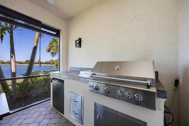 view of patio with exterior kitchen, a water view, and grilling area