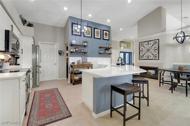 kitchen featuring a breakfast bar area, a sink, white cabinetry, appliances with stainless steel finishes, and a tiled fireplace