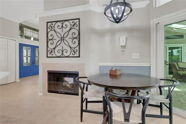 dining space with light tile patterned floors, a fireplace, ornamental molding, and a chandelier