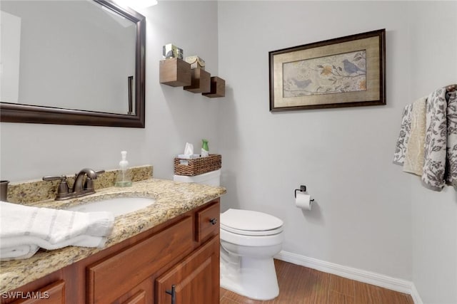 bathroom featuring toilet, baseboards, wood finished floors, and vanity