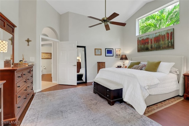 bedroom with ensuite bathroom, high vaulted ceiling, wood finished floors, a ceiling fan, and baseboards