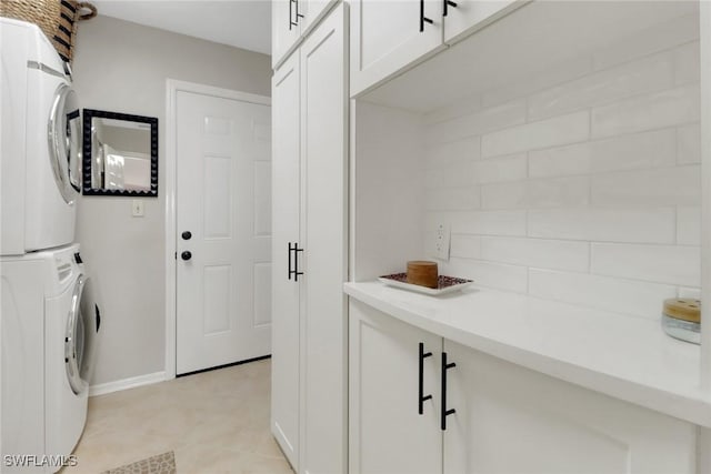 washroom featuring cabinet space, baseboards, and stacked washer / drying machine