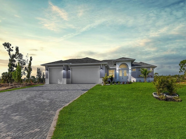 prairie-style home with decorative driveway, a yard, a garage, and stucco siding