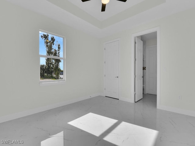 spare room featuring baseboards, a raised ceiling, marble finish floor, and a ceiling fan