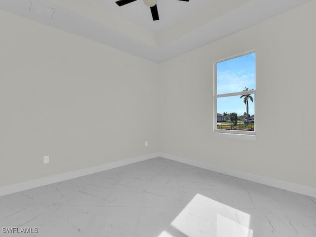 spare room featuring a raised ceiling, a ceiling fan, baseboards, and marble finish floor