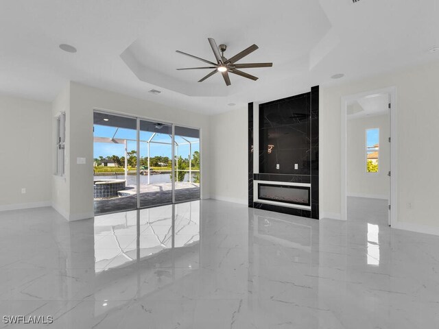 unfurnished room featuring a tray ceiling, baseboards, and marble finish floor