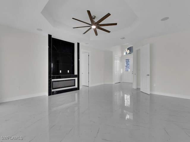 unfurnished living room with a raised ceiling, baseboards, and marble finish floor