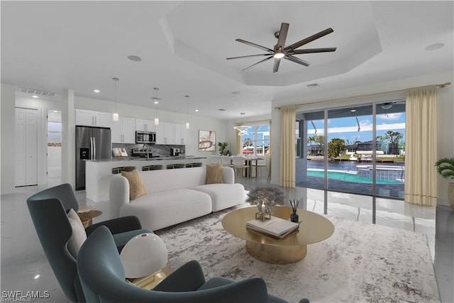 living area with a tray ceiling, marble finish floor, visible vents, and a ceiling fan