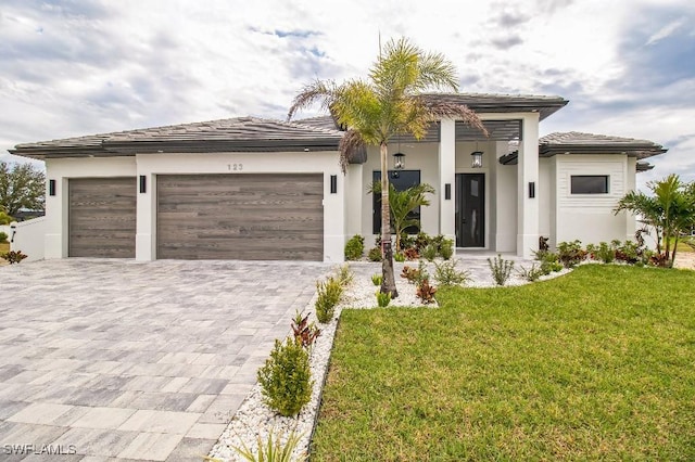 prairie-style home with a garage, a tiled roof, decorative driveway, stucco siding, and a front lawn