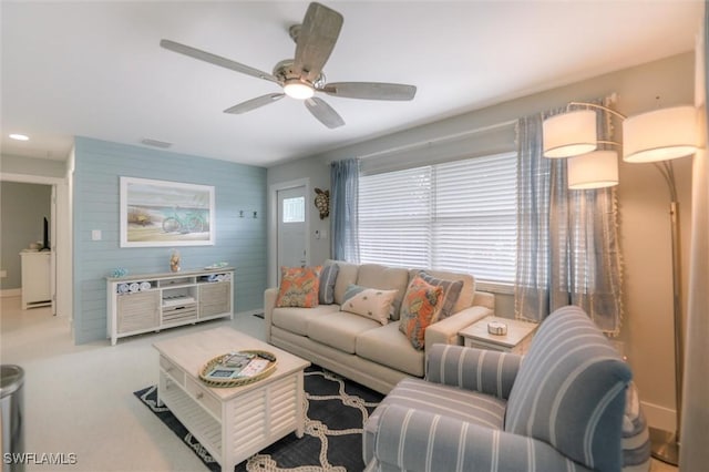 living room with wooden walls, visible vents, a ceiling fan, an accent wall, and carpet floors