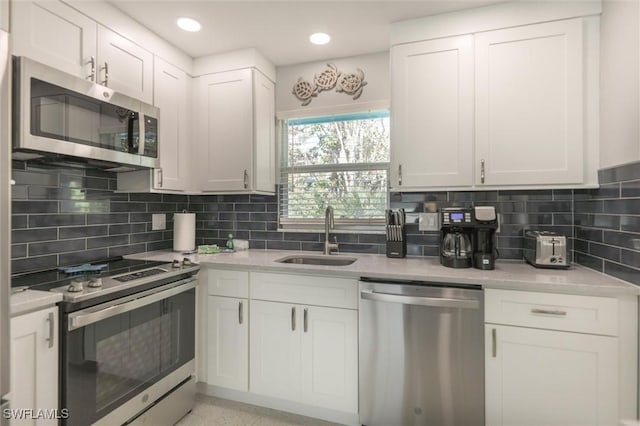 kitchen with appliances with stainless steel finishes, white cabinets, a sink, and decorative backsplash