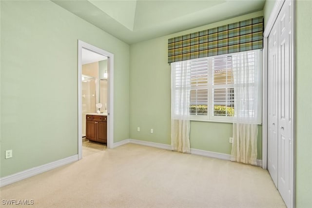 unfurnished bedroom featuring light carpet, connected bathroom, baseboards, and a closet