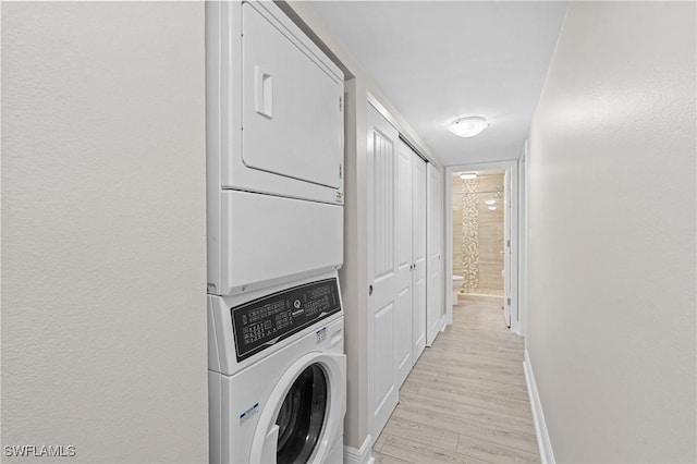 laundry room featuring baseboards, stacked washer and clothes dryer, and light wood-style floors