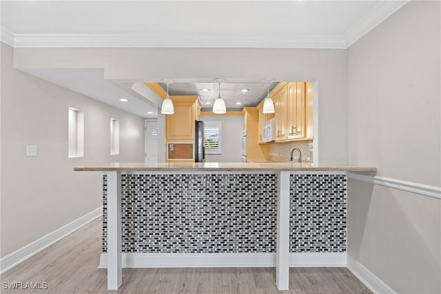 kitchen featuring baseboards, white microwave, ornamental molding, a kitchen breakfast bar, and light brown cabinets