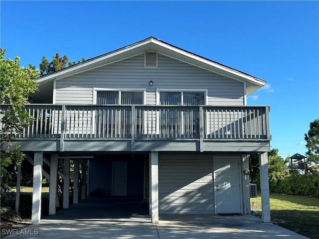 rear view of property featuring a carport, concrete driveway, and a wooden deck