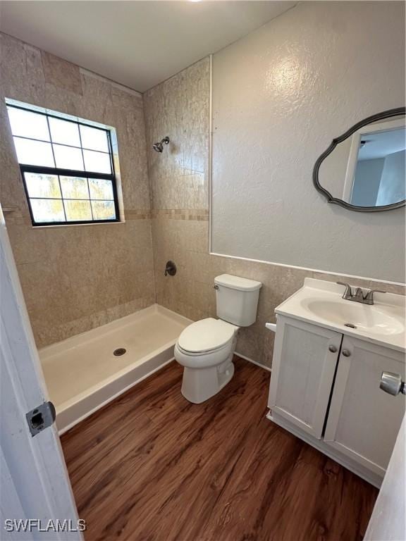 full bath with toilet, vanity, wood finished floors, and tiled shower