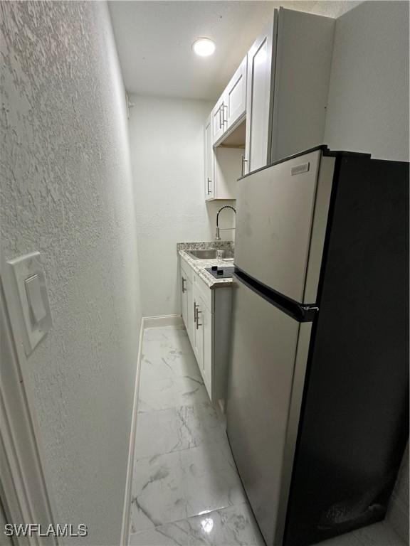 kitchen with marble finish floor, a textured wall, freestanding refrigerator, a sink, and baseboards