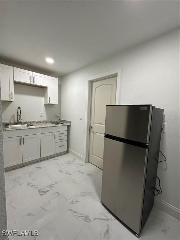 kitchen with marble finish floor, baseboards, a sink, and freestanding refrigerator