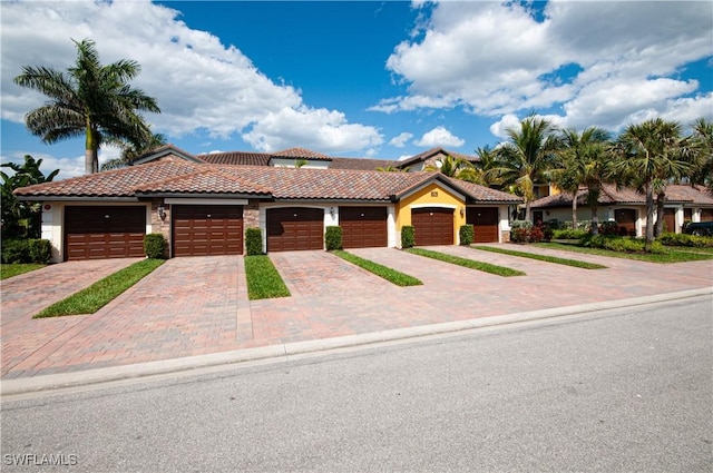 view of front facade with a garage, stucco siding, decorative driveway, and a tiled roof