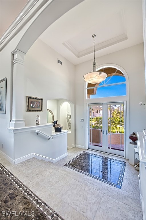 foyer entrance featuring visible vents, arched walkways, a raised ceiling, baseboards, and a high ceiling