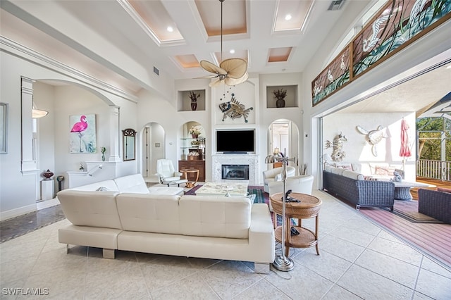 living room featuring built in features, arched walkways, a towering ceiling, a glass covered fireplace, and coffered ceiling