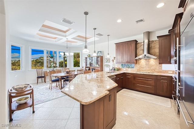 kitchen with backsplash, visible vents, wall chimney range hood, and a peninsula