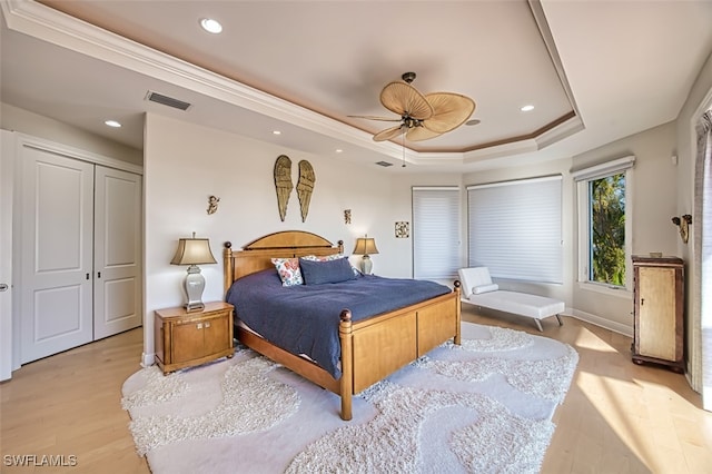 bedroom with recessed lighting, visible vents, ornamental molding, a tray ceiling, and light wood finished floors