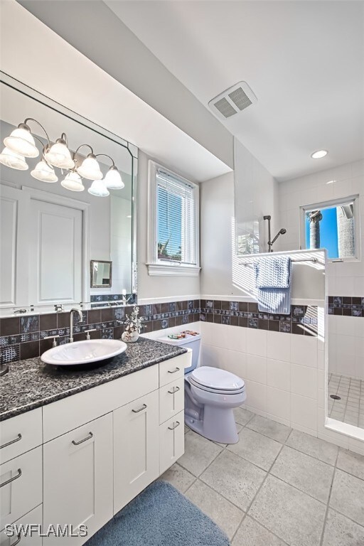 full bathroom with tile walls, visible vents, toilet, vanity, and walk in shower