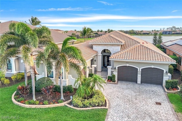 mediterranean / spanish-style home with decorative driveway, stucco siding, an attached garage, fence, and a tiled roof