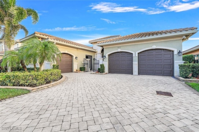 mediterranean / spanish home with an attached garage, a tiled roof, decorative driveway, and stucco siding