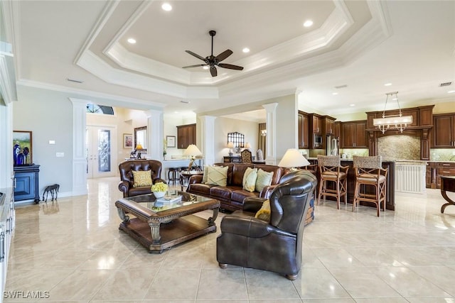 living area with crown molding, a raised ceiling, a ceiling fan, and ornate columns