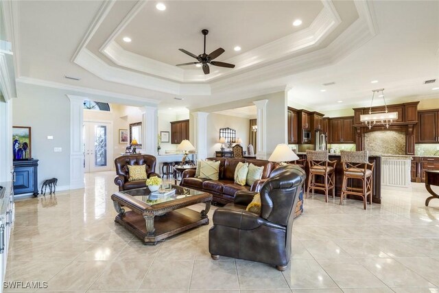 living area featuring crown molding, a raised ceiling, ceiling fan, and ornate columns