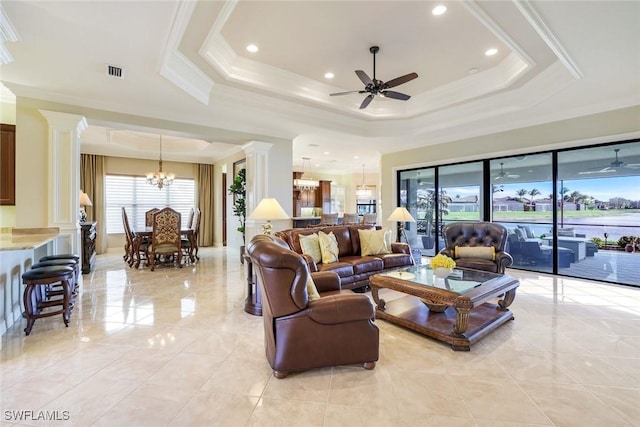 living room featuring decorative columns, visible vents, a tray ceiling, crown molding, and ceiling fan with notable chandelier