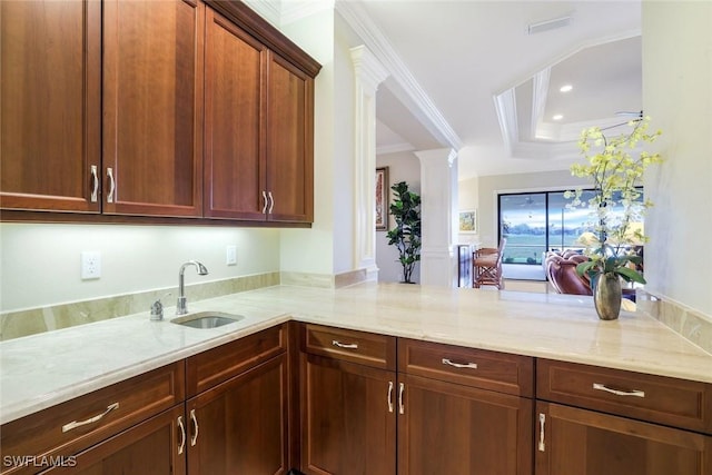 kitchen with light stone counters, a tray ceiling, crown molding, a sink, and ornate columns