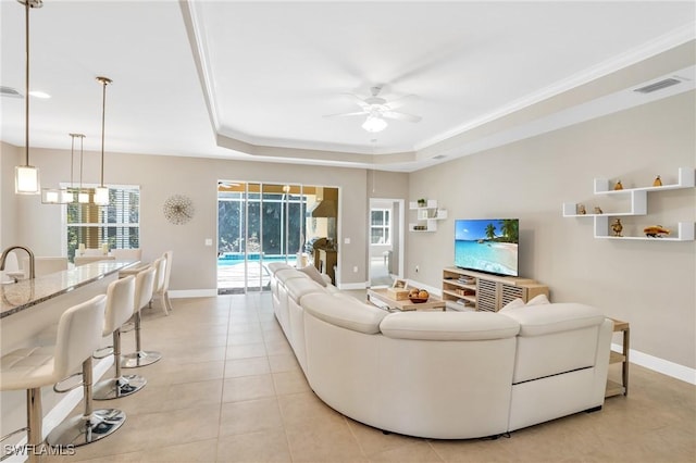 living room featuring baseboards, a raised ceiling, a ceiling fan, and crown molding