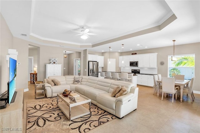 living area featuring a tray ceiling, ornamental molding, light tile patterned floors, and ceiling fan