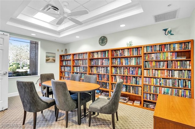 sitting room with visible vents, a tray ceiling, carpet flooring, ceiling fan, and wall of books