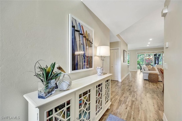 hall featuring a textured wall, recessed lighting, light wood-style flooring, and baseboards