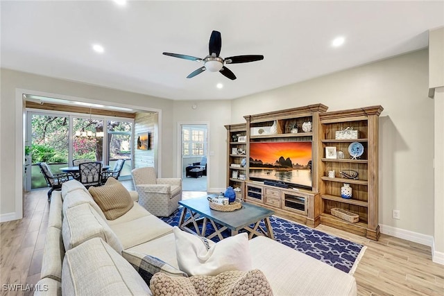 living room with baseboards, ceiling fan with notable chandelier, and light wood-style floors