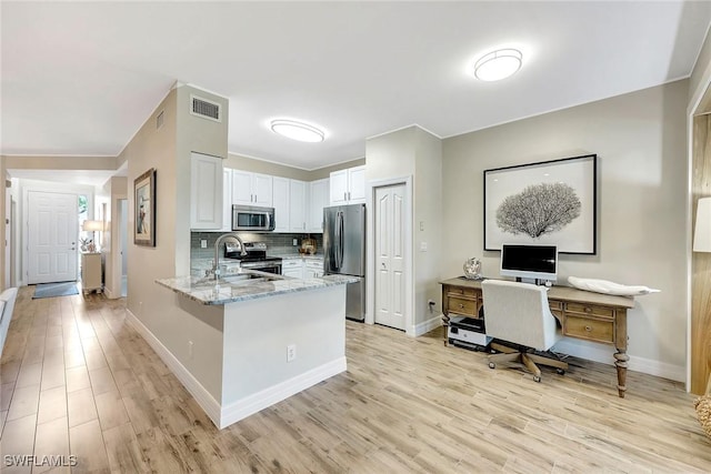 kitchen featuring light stone counters, stainless steel appliances, a peninsula, a sink, and white cabinets