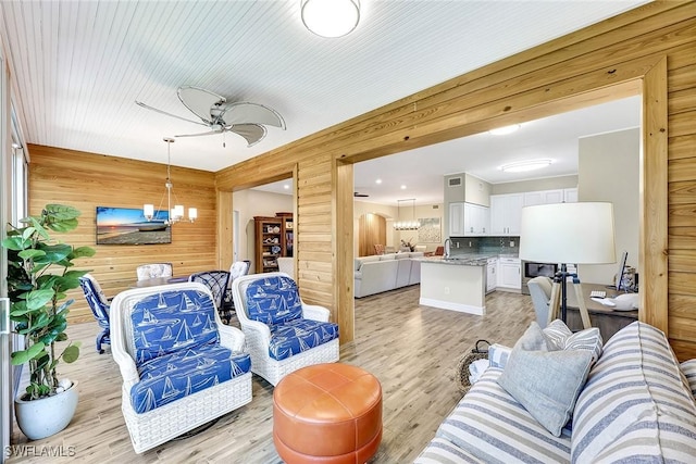 living room featuring ceiling fan with notable chandelier, wood walls, and light wood-style flooring