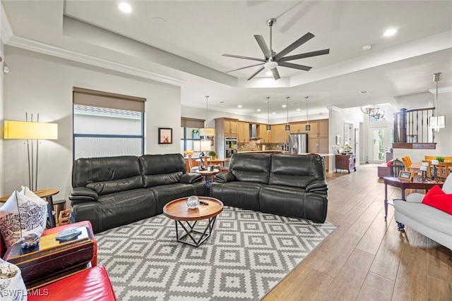 living room with ceiling fan with notable chandelier, recessed lighting, a raised ceiling, and light wood-style floors