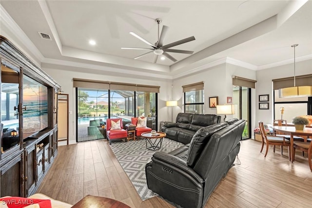 living room featuring light wood-style floors, visible vents, a raised ceiling, and a sunroom